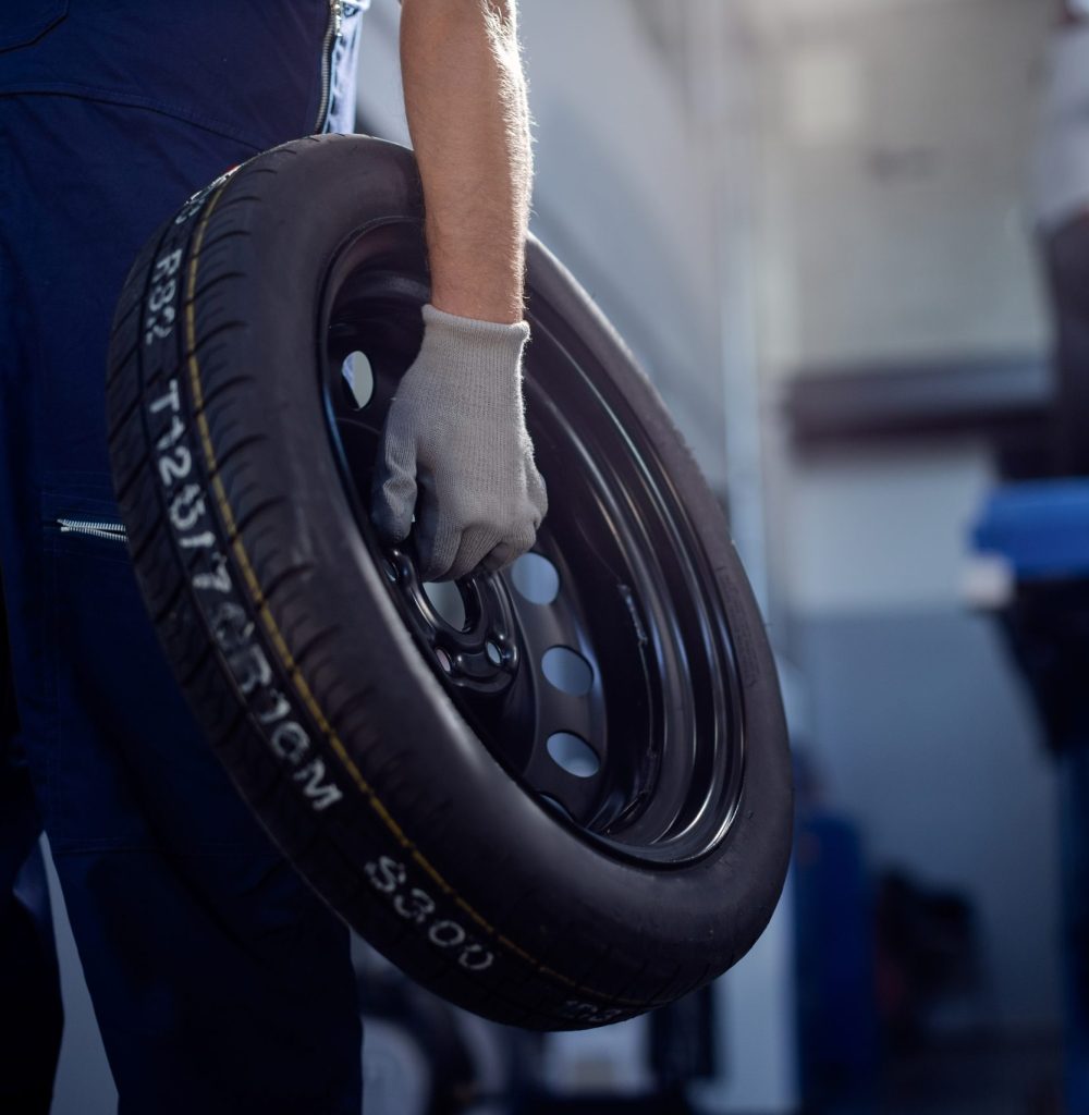 Unrecognizable mechanic holding car tire while working in auto repair shop.